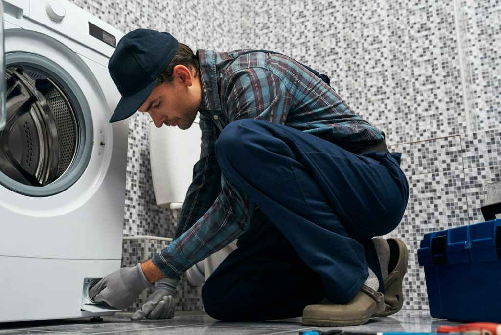 A man fixing a washing machine in a bathroom, exploring the future of industrial electrical services.