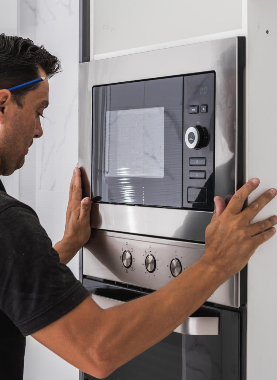 A man installing a microwave oven in a kitchen.