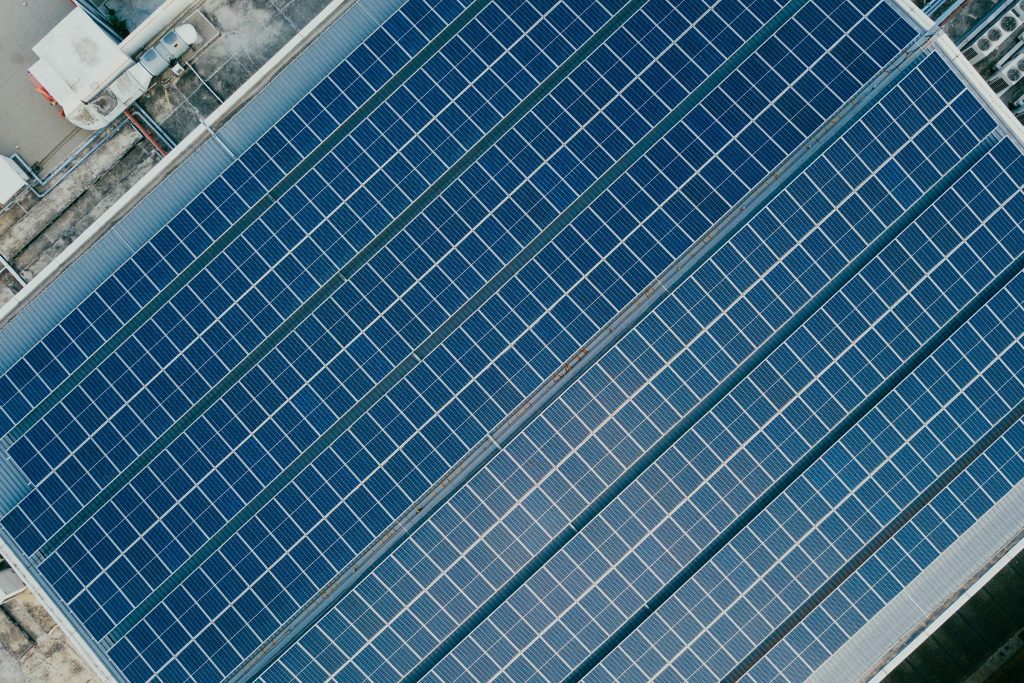 Aerial view of a large rooftop adorned with blue REC Alpha Pure Series solar panels, meticulously aligned in rows and surrounded by visible rooftop structures and equipment.